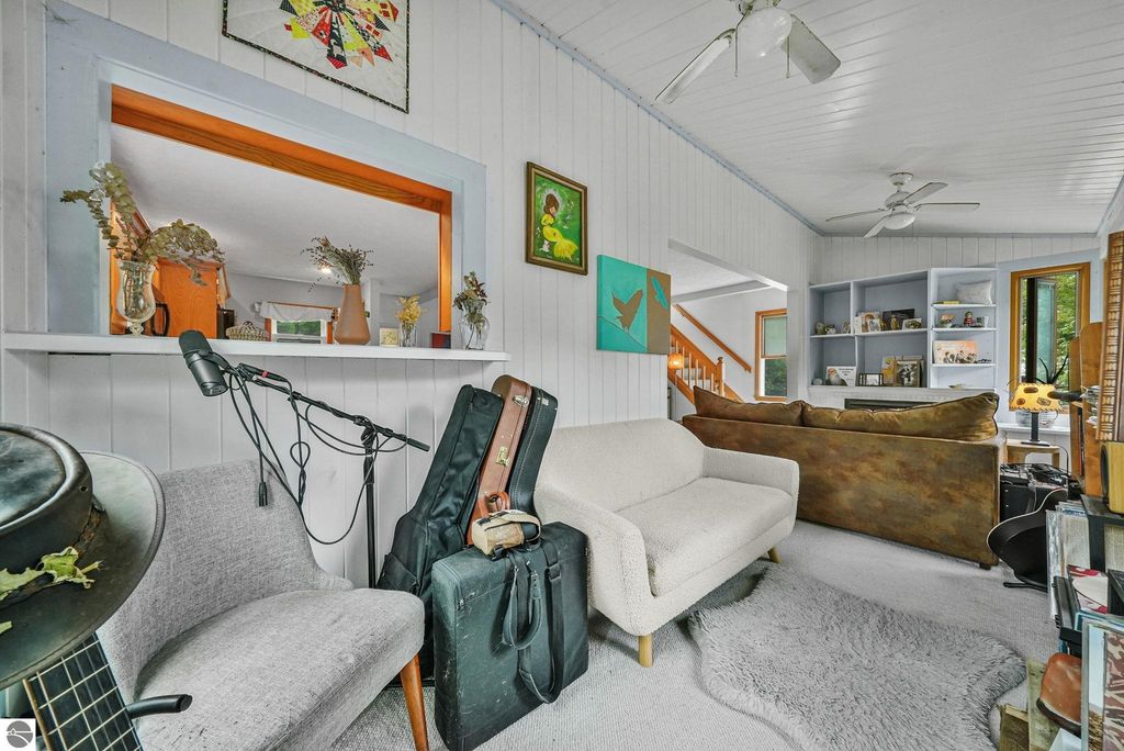 Cozy living room with a white sofa, guitar, and musical equipment, showcasing a bright, inviting space in a farmhouse near Leland, MI, featuring wood paneling and decorative art.