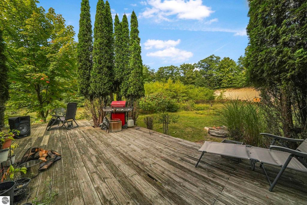 Deck area with lounge chairs and a grill, surrounded by trees and lush greenery, showcasing the outdoor space of the farmhouse at 5361 N Manitou Trail, Leland, MI.