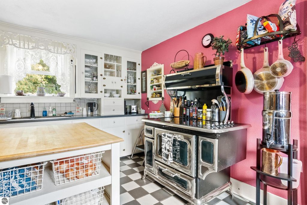Victorian-style kitchen featuring a vintage stove, white cabinetry, and a pink accent wall, with a wooden countertop and various kitchen utensils displayed.