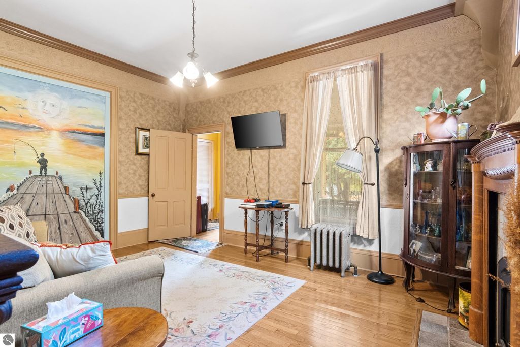 Victorian living room featuring original wood trim, a decorative mural of a fishing scene, modern TV, and antique furnishings, highlighting the charm of the 1880 home in Onekama, MI.