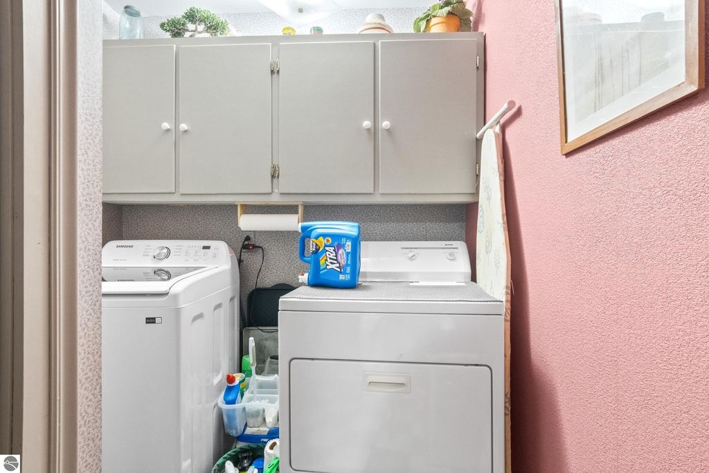 Laundry room featuring a Samsung washer and dryer, gray cabinets, cleaning supplies, and a decorative touch with a framed picture on the wall, highlighting the functional space in the Victorian home at 8195 Fifth Street, Onekama, MI.