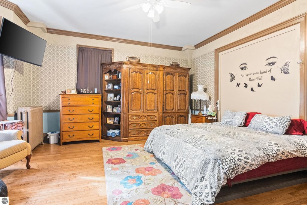 Victorian-style bedroom featuring a large bed with patterned bedding, antique wooden furniture, decorative wall art, and a cozy atmosphere, reflecting the charm of the 1880 home in Onekama, MI.