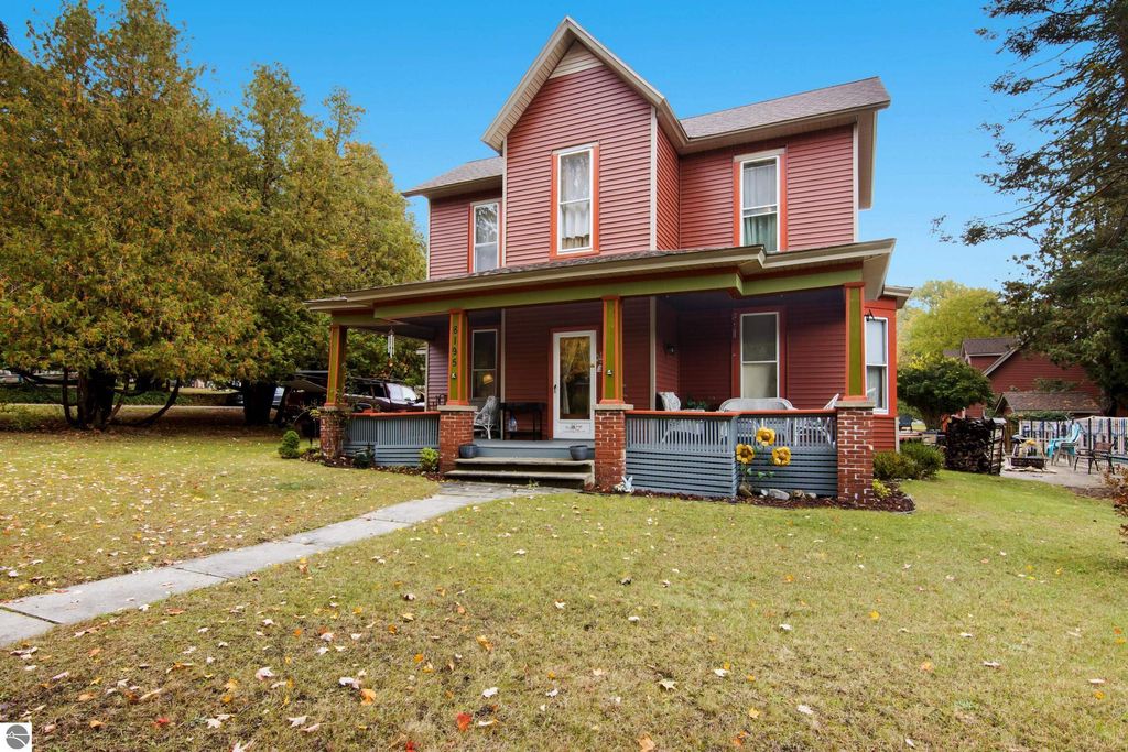 Victorian-style home at 8195 Fifth Street, Onekama, MI, featuring original wood trim, inviting porch, and landscaped yard with fall foliage, showcasing character and modern updates.