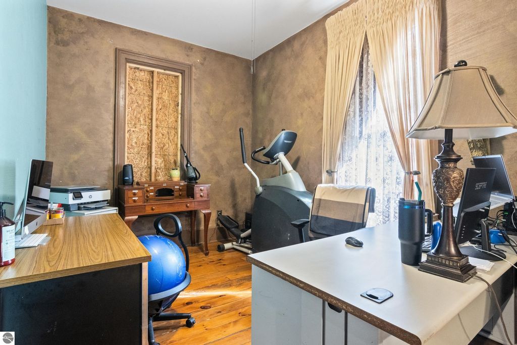Home office interior featuring a vintage desk, exercise equipment, and modern office supplies, showcasing the blend of historical charm and contemporary functionality in the Victorian home at 8195 Fifth Street, Onekama, MI.