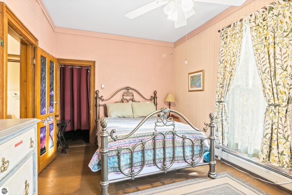 Victorian bedroom featuring a metal bed frame with colorful bedding, floral curtains, and wooden accents, reflecting the charm of the 1880 home in Onekama, MI.