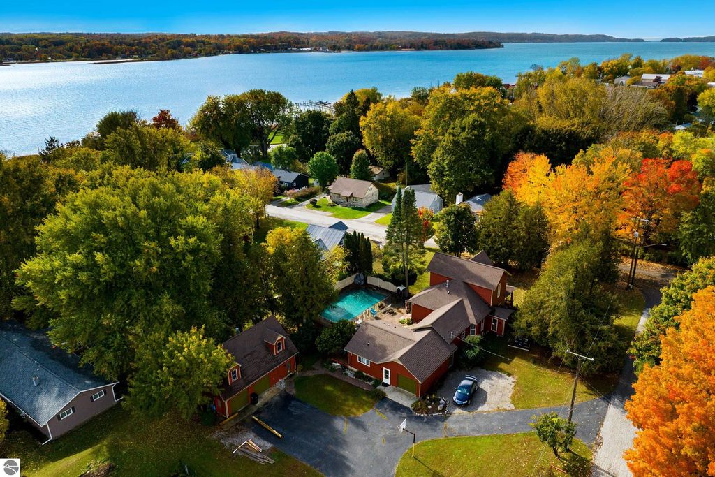 Aerial view of a Victorian-style home with a pool, surrounded by vibrant autumn foliage and near Portage Lake, showcasing the property’s expansive yard and nearby residential area in Onekama, MI.