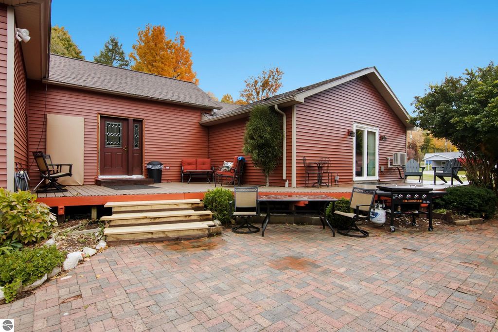 Victorian-style home exterior with red siding, wooden deck, patio seating, and grill, surrounded by landscaped garden in Onekama, MI.