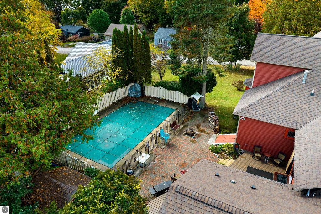 Aerial view of a Victorian home in Onekama, MI, showcasing a covered in-ground pool, patio area with seating, and surrounding lush greenery, highlighting the property's charming outdoor space.
