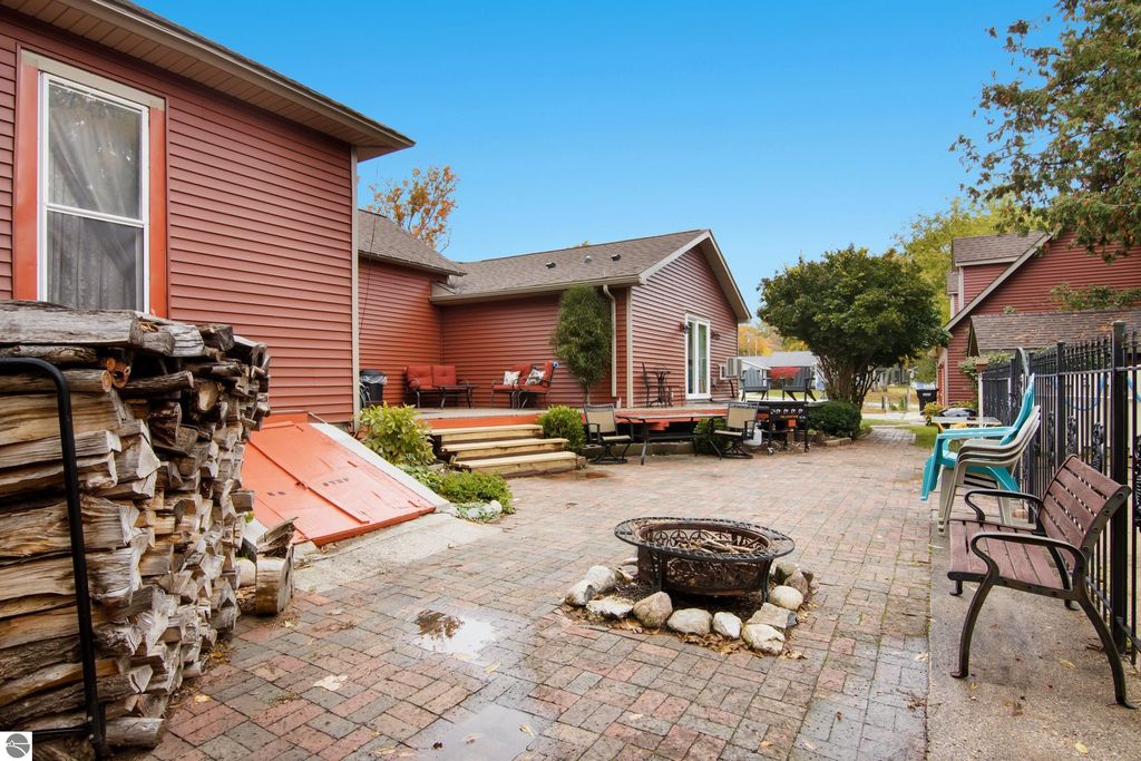 Victorian-style home backyard in Onekama, featuring a brick patio, fire pit, wood stack, and outdoor seating area with modern updates and landscaping.