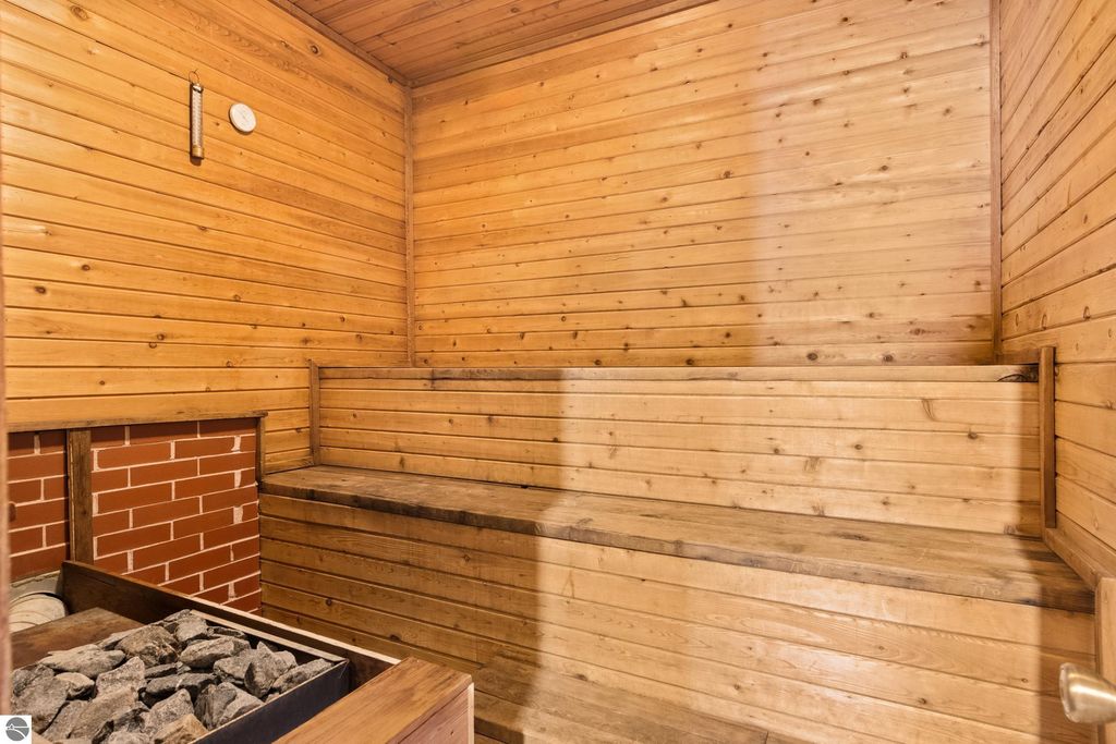 In-home sauna with wooden walls, benches, and stone heater, highlighting relaxation features of the Victorian property in Onekama, MI.