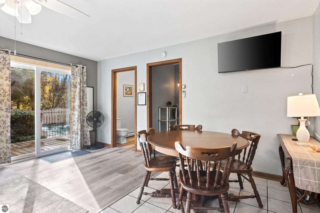 Dining area with wooden table and chairs, modern decor, large sliding door leading to backyard, visible in-ground pool, and warm lighting, showcasing the inviting atmosphere of the Victorian home for sale in Onekama, MI.