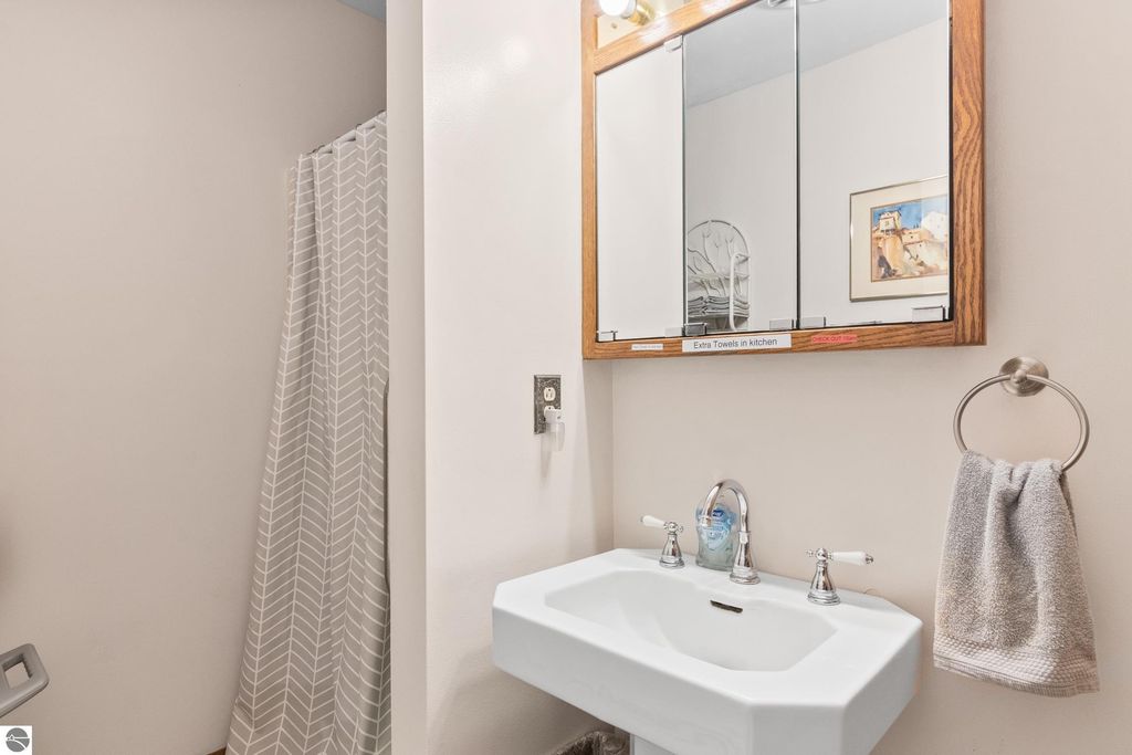 Bathroom with a white sink, mirrored cabinet, and shower curtain, featuring modern fixtures and a towel rack, reflecting the updated amenities of the Victorian home in Onekama, MI.