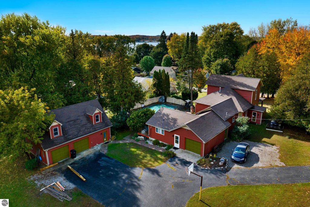 Aerial view of a Victorian-style home in Onekama, Michigan, featuring a red exterior, surrounding trees, an in-ground pool, and a self-contained apartment, set on a spacious lot near Portage Lake.