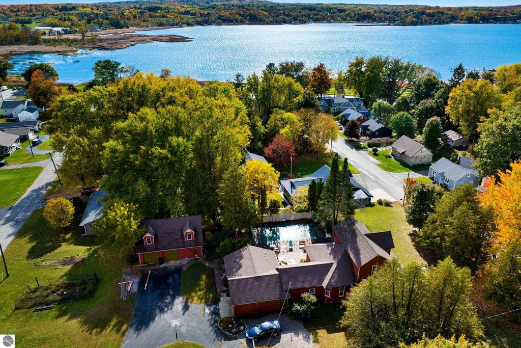 Aerial view of a Victorian-style home with a pool in Onekama, MI, surrounded by vibrant fall foliage, near Portage Lake and residential neighborhood.