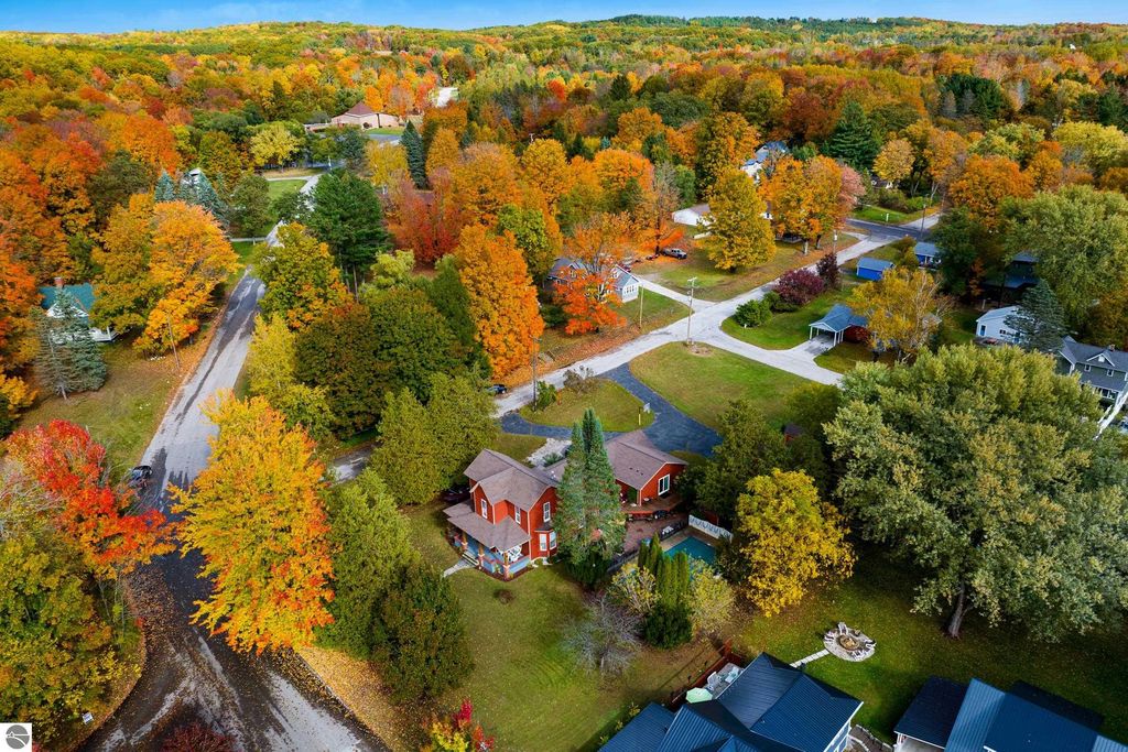 Aerial view of a Victorian-style home surrounded by vibrant autumn foliage in Onekama, MI, showcasing the property's spacious yard, nearby roads, and colorful trees.