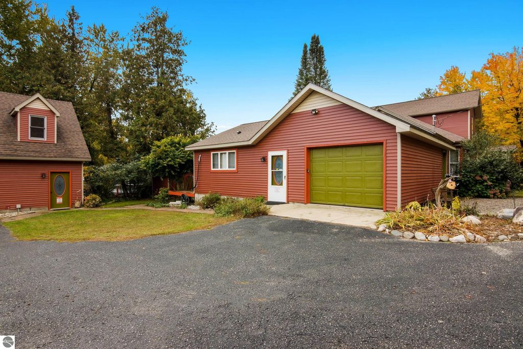 Victorian-style home at 8195 Fifth Street, Onekama, MI, featuring red exterior, green garage door, landscaped yard, and surrounding trees, showcasing its historic charm and modern updates.