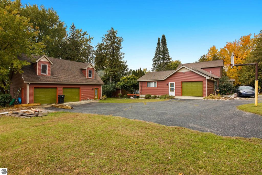 Victorian-style home exterior with red siding, green garage doors, and a basketball hoop, surrounded by trees and lawn, located at 8195 Fifth Street, Onekama, MI, near a resort-style backyard and in-ground pool.