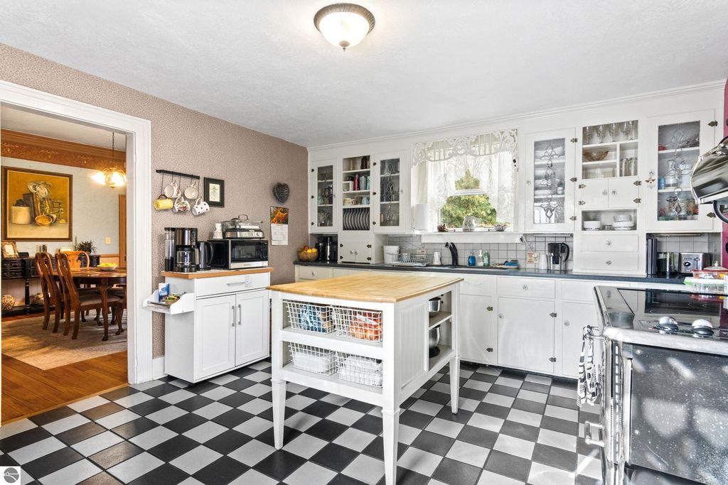 Victorian-style kitchen featuring white cabinetry, a central island with storage, and a black-and-white checkered floor, showcasing a blend of classic charm and modern amenities.