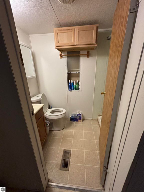 Bathroom interior featuring a toilet, wooden cabinet above a sink, and storage space with toiletries, showcasing the functional layout of the 5013 Turner Pine Drive property in Prescott, MI.
