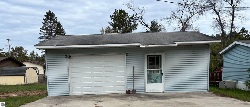 Detached two-car garage with light blue siding, concrete driveway, and door entrance, situated near residential homes in Prescott, MI, as part of the property listing at 5013 Turner Pine Drive.