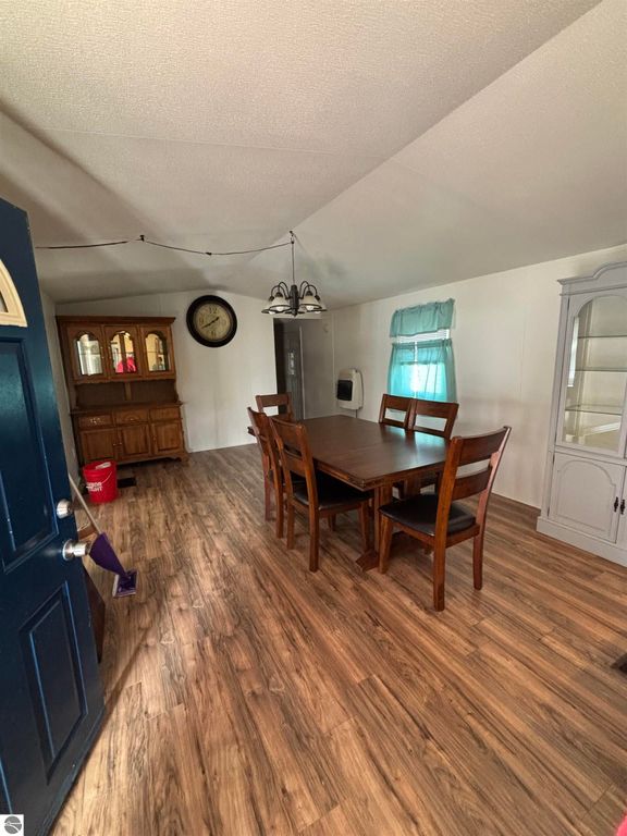 Interior view of a manufactured home featuring a dining area with wooden table and chairs, a wall clock, and a china cabinet, showcasing the spacious layout and natural light.