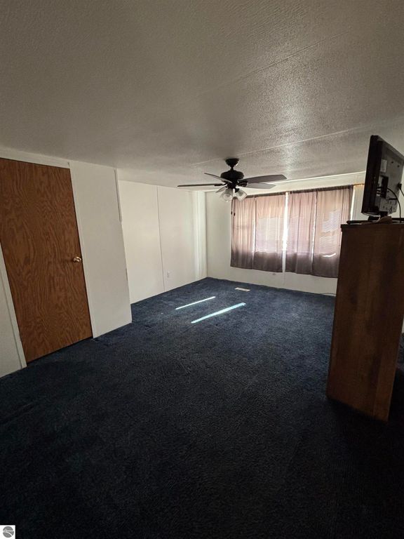 Interior view of a two-bedroom manufactured home in Prescott, MI, featuring a ceiling fan, carpeted flooring, and natural light from window curtains.