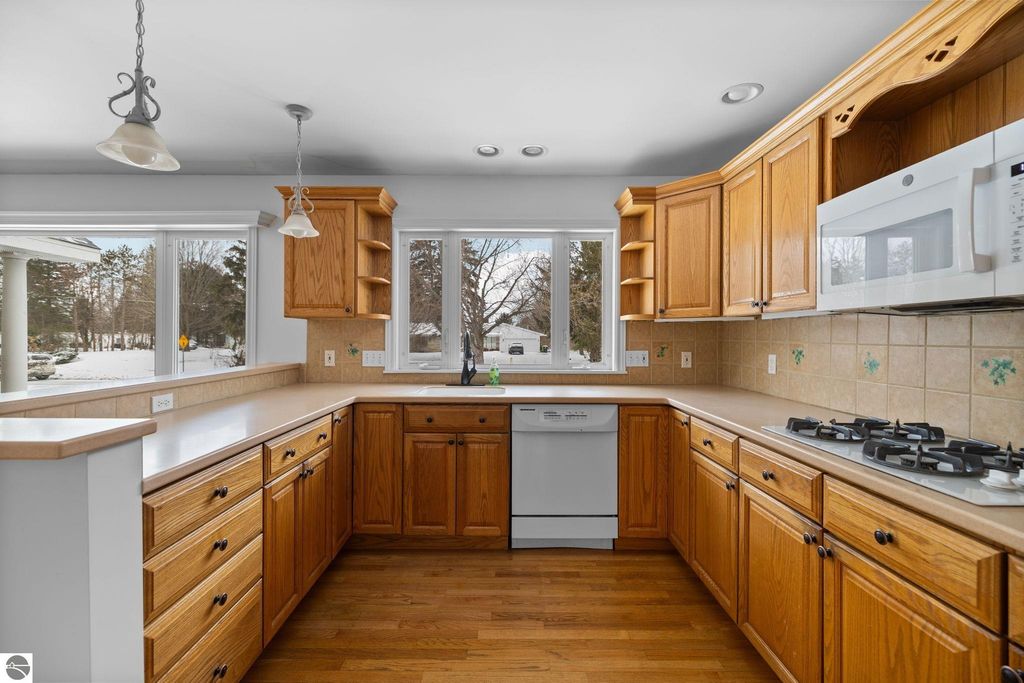 Bright kitchen featuring wooden cabinets, white appliances, and a decorative floral backsplash, showcasing a spacious layout ideal for gatherings in the Traverse City home at 109 Boughey Street.