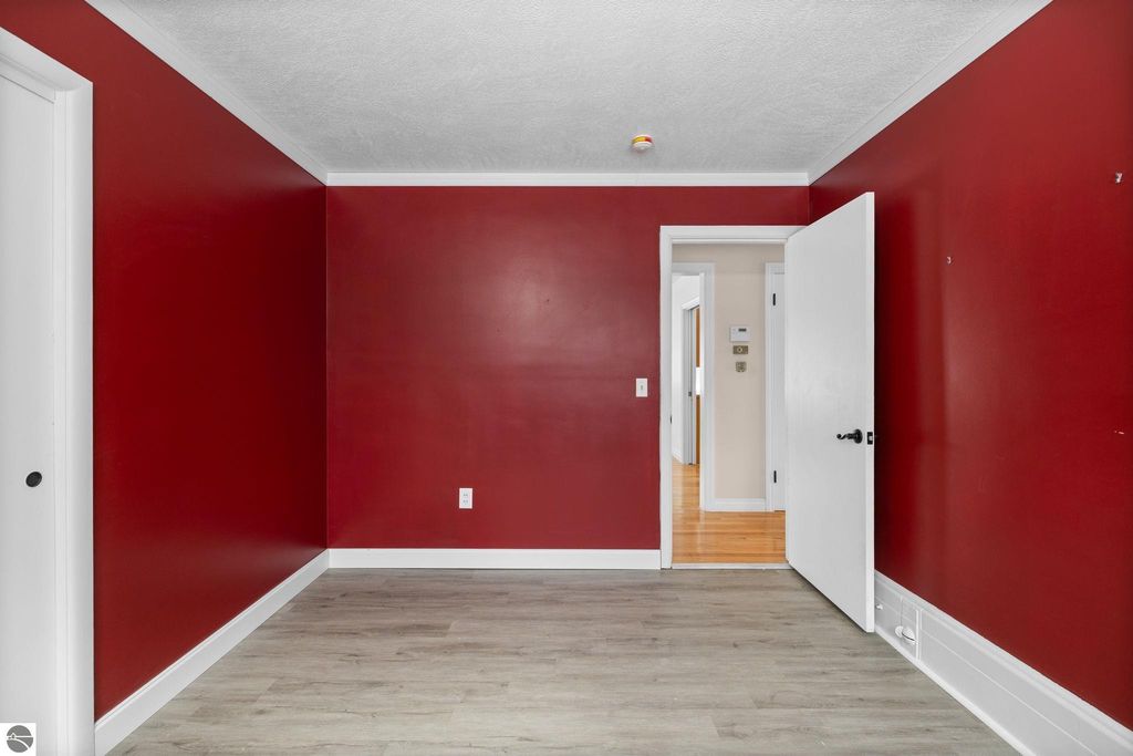 Bright red accent wall in a spacious room with large windows, wooden flooring, and a white shelving unit, showcasing a cozy interior design suitable for a home in Traverse City, MI.