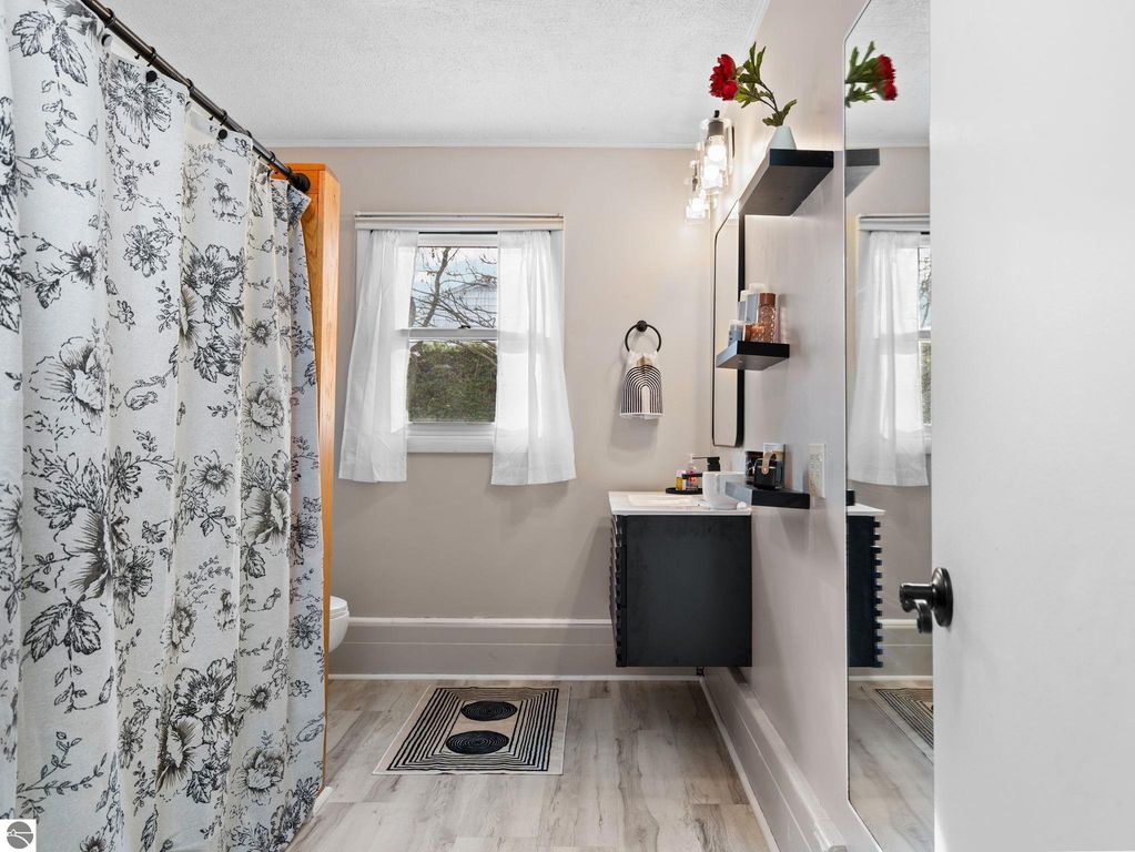 Bright and airy bedroom featuring large windows with autumn views, light hardwood flooring, and built-in white closets, showcasing the inviting interior of the Traverse City home at 109 Boughey Street.