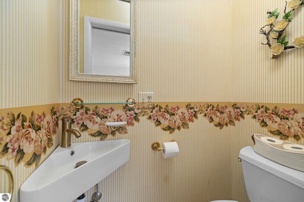 Bathroom vanity with dual sinks, modern faucet, and decorative floral wallpaper, showcasing a bright and inviting space in a Traverse City home listing.
