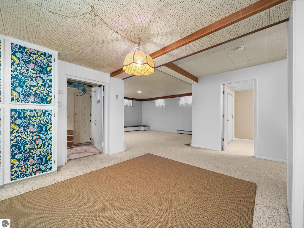 Finished basement room with beige walls, carpeted floor, and white double doors, showcasing potential for additional living space in a Traverse City home.