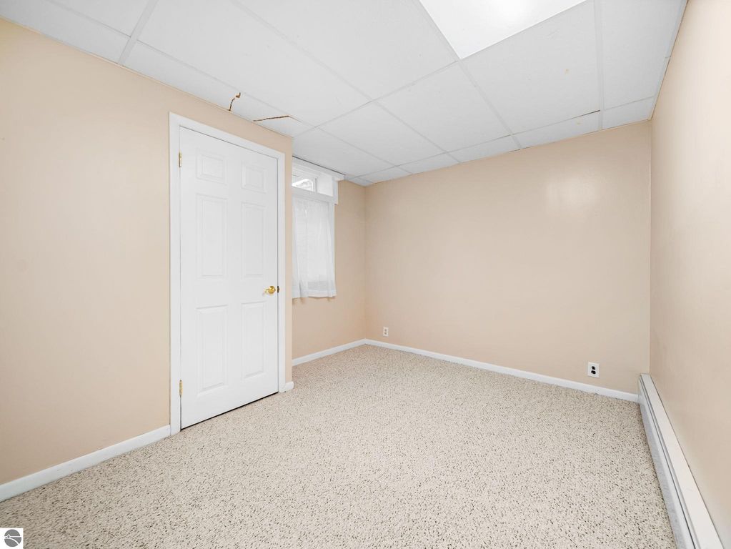 Laundry room in finished basement featuring washer, dryer, utility sink, and privacy curtain, with patterned flooring and white walls, in Traverse City ranch home.