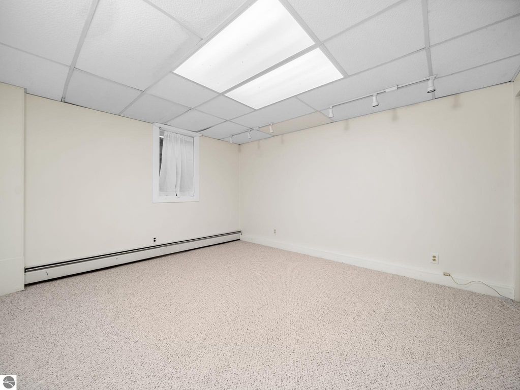 Laundry room in Traverse City home featuring white washer and dryer, utility sink, and storage cart, with natural light from windows above, and patterned flooring.