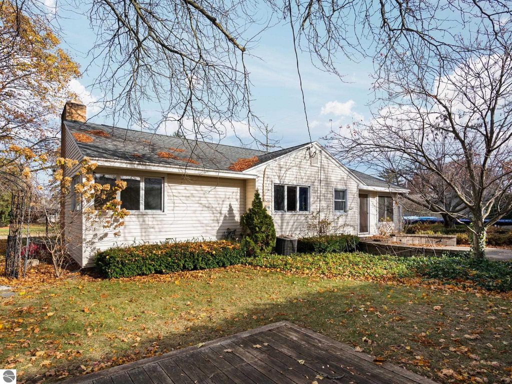 Backyard view of 109 Boughey Street, Traverse City, featuring a paved patio, autumn foliage, and landscaped garden with trees and shrubs, highlighting outdoor living space.