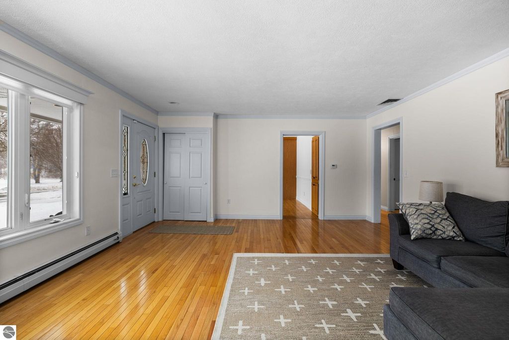 Living room in Traverse City ranch home featuring hardwood floors, green walls, a cozy fireplace, built-in bookcases, and large windows overlooking the front yard.