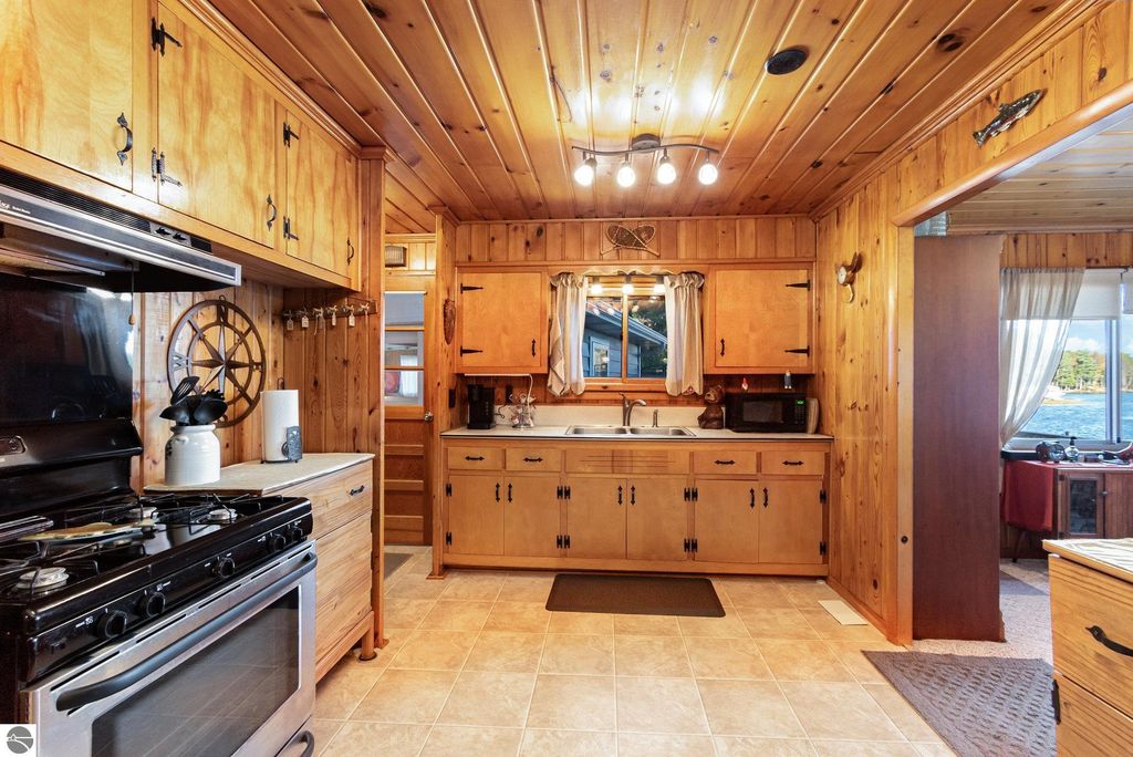 Remodeled kitchen in a knotty-pine home featuring wooden cabinetry, a gas stove, and a view of Big Island Lake, emphasizing rustic charm and cozy atmosphere.