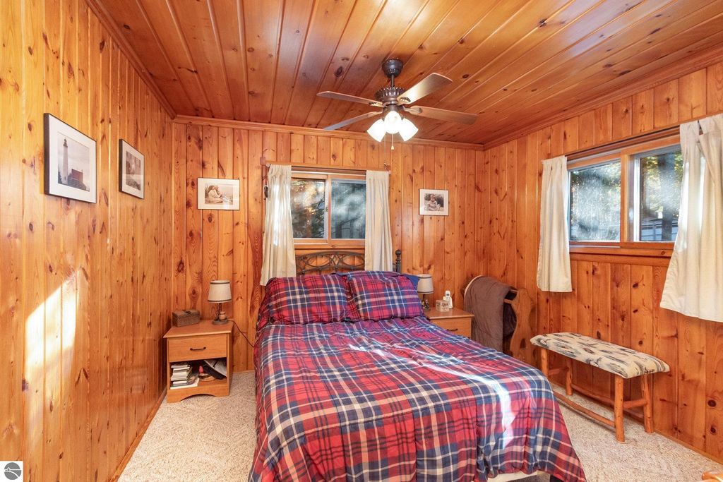 Cozy bedroom featuring knotty pine paneling, plaid bedding, and natural light from windows, highlighting a rustic retreat atmosphere near Big Island Lake.