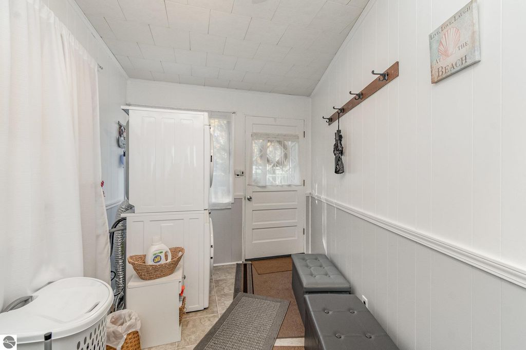 Interior view of a laundry room with a white washer and dryer, a door leading outside, a gray bench, and storage baskets, reflecting the cozy and functional design of the home at 2096 Timber Trail, National City, MI.