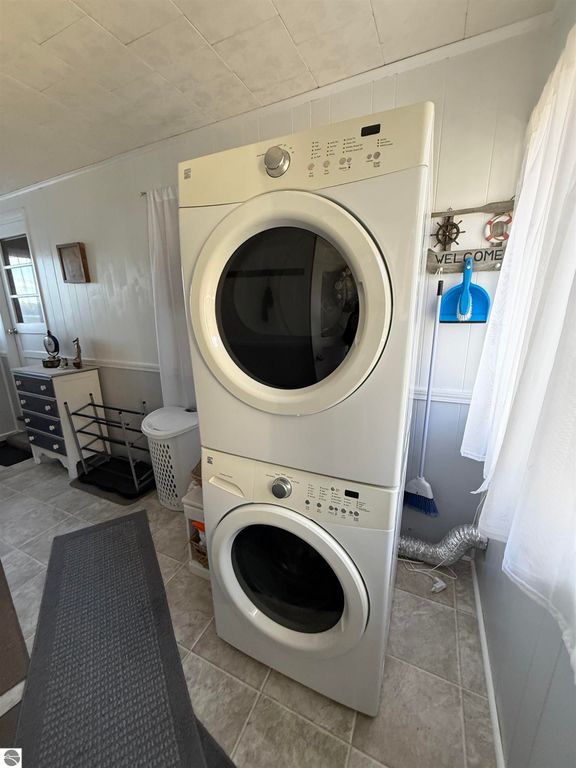 Stacked washer and dryer in a bright, airy laundry area with white walls and decorative elements, showcasing convenient home amenities for the property at 2096 Timber Trail, National City, MI.