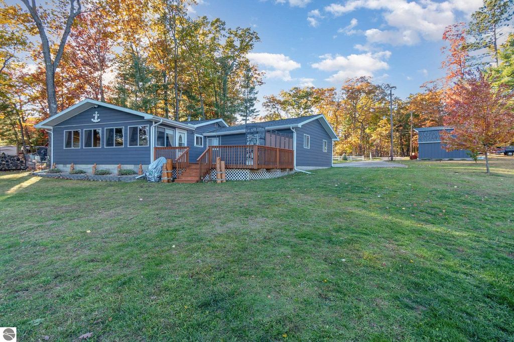 Beautifully remodeled knotty-pine home at 2096 Timber Trail, National City, MI, featuring a spacious deck, panoramic all-season room, and landscaped yard near Big Island Lake.
