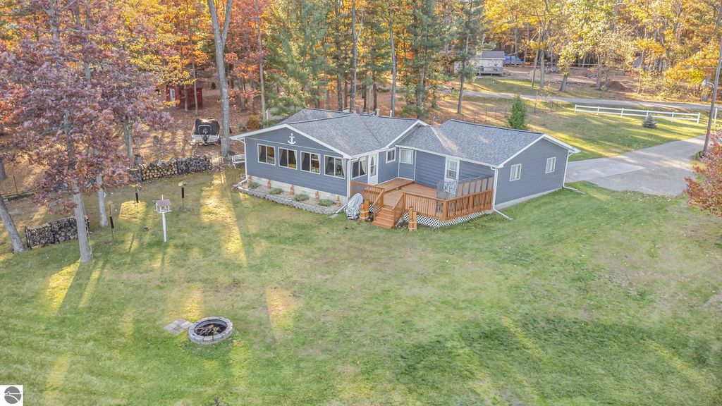 Aerial view of a beautifully remodeled knotty-pine home at 2096 Timber Trail, surrounded by trees, featuring a spacious deck, fire pit, and landscaped yard near Big Island Lake in National City, MI.