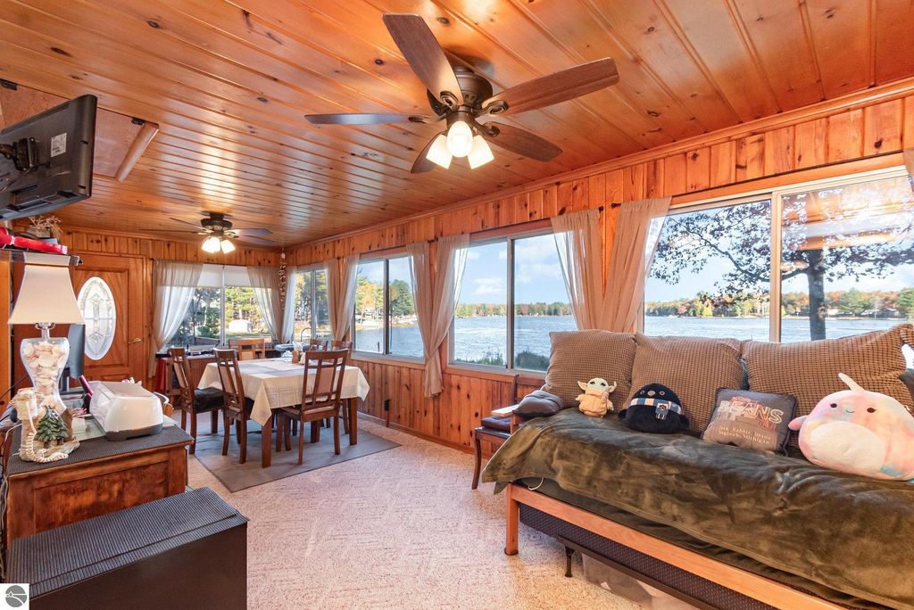 Cozy knotty-pine interior of a lakefront home, featuring a dining area with a table and chairs, plush seating with decorative pillows, large windows showcasing scenic lake views, and warm wooden accents, highlighting the property's inviting atmosphere near Big Island Lake.