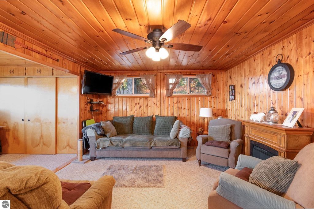 Cozy living room with knotty pine walls, comfortable seating, wall-mounted TV, and a decorative fireplace, showcasing a warm and inviting atmosphere in the remodeled home at 2096 Timber Trail, National City, MI.