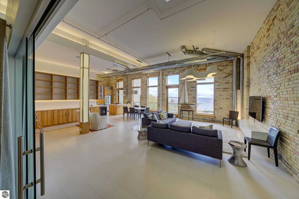 Modern downtown condo interior featuring open layout, large windows with bay views, exposed brick walls, and contemporary furnishings, showcasing the luxurious living space at 237 E Front Street, Traverse City, MI.