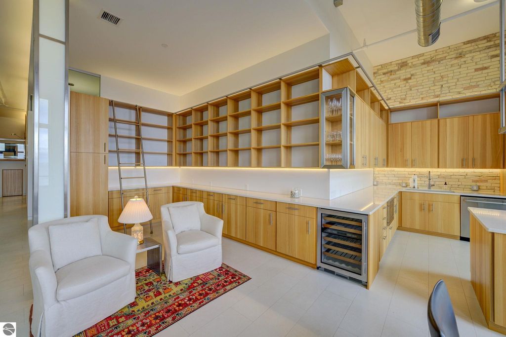 Modern kitchen with wooden cabinetry, integrated appliances, and a cozy seating area featuring white armchairs and a decorative rug, highlighting the contemporary design of the downtown condo at 237 E Front Street, Traverse City.