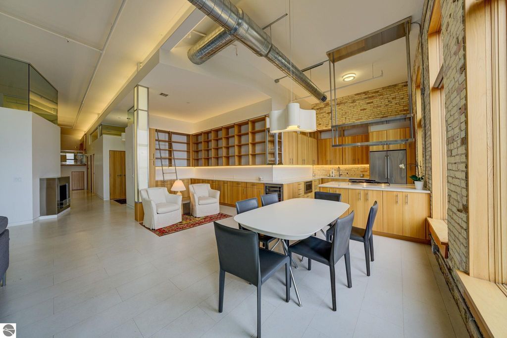 Modern downtown condo interior featuring an open layout, sleek kitchen with wooden cabinetry, dining area with a white table and black chairs, and large windows providing natural light, located at 237 E Front Street, Traverse City, MI.