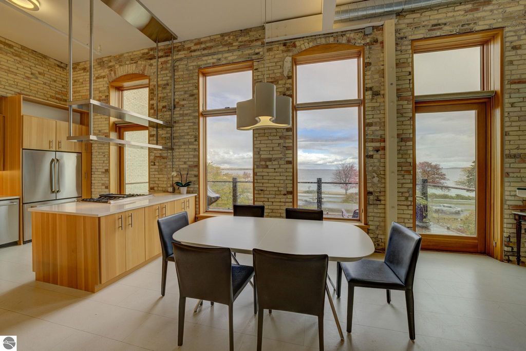 Modern kitchen and dining area featuring large windows with bay views, sleek cabinetry, and a contemporary dining table, ideal for the downtown Traverse City condo listing at 237 E Front Street.