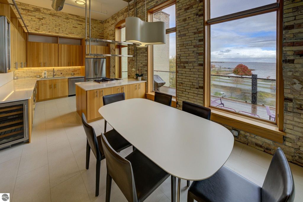 Modern kitchen and dining area featuring sleek cabinetry, stainless steel appliances, and large windows with views of the bay, highlighting the contemporary design of the downtown Traverse City condo at 237 E Front Street.