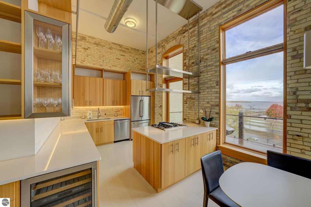 Modern kitchen with wooden cabinetry, stainless steel appliances, and large windows showcasing views of the bay in a downtown Traverse City condo.