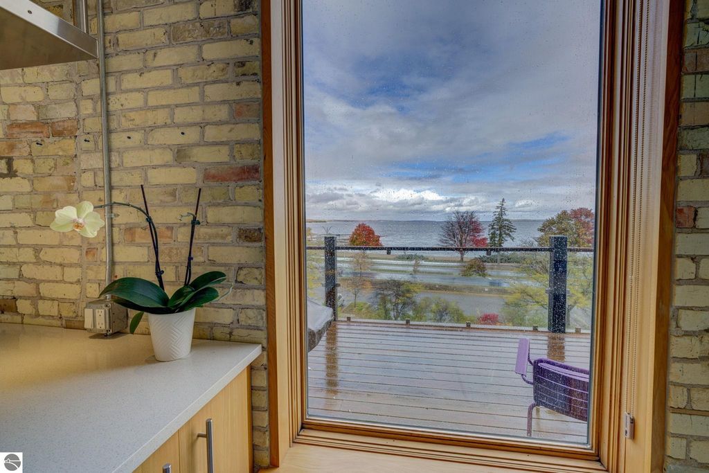 Modern condo interior featuring a potted orchid on a countertop, with a large window showcasing scenic views of Traverse City’s bay and waterfront, highlighting the architectural design and natural light.